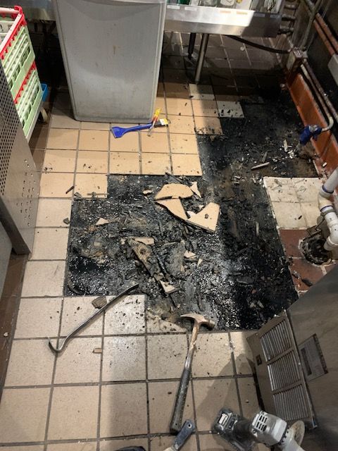Kitchen floor with burned debris and ashes near stainless steel equipment and tiles