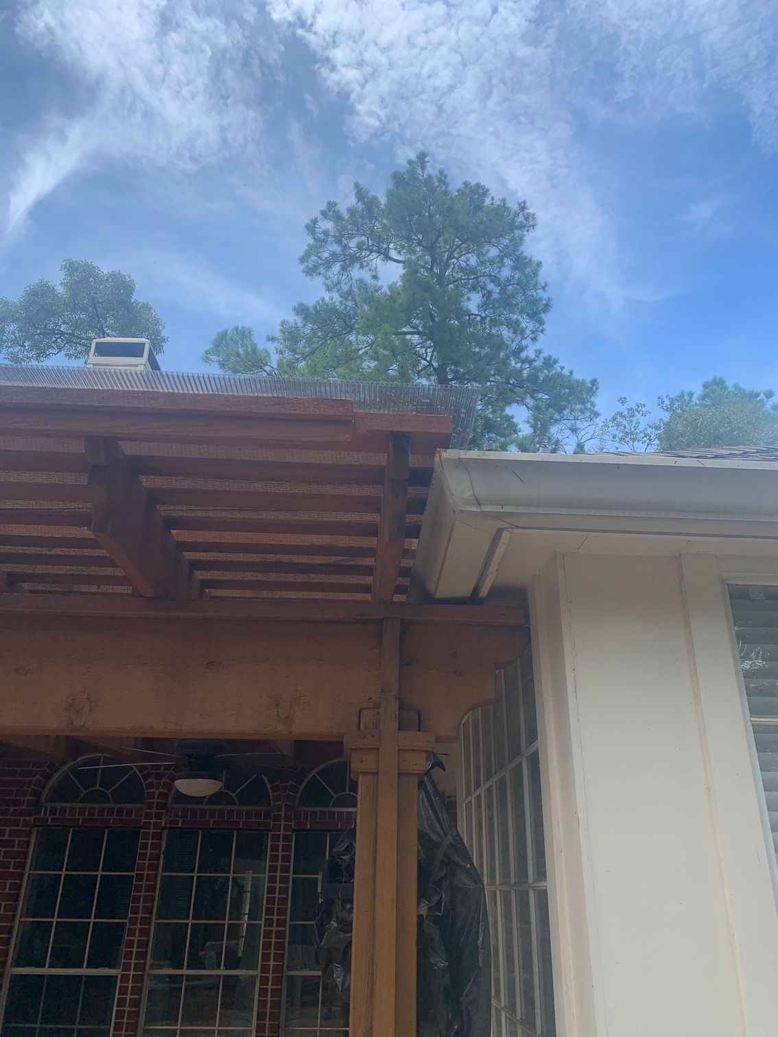 House roof and porch with wooden overhang beneath a blue sky and trees