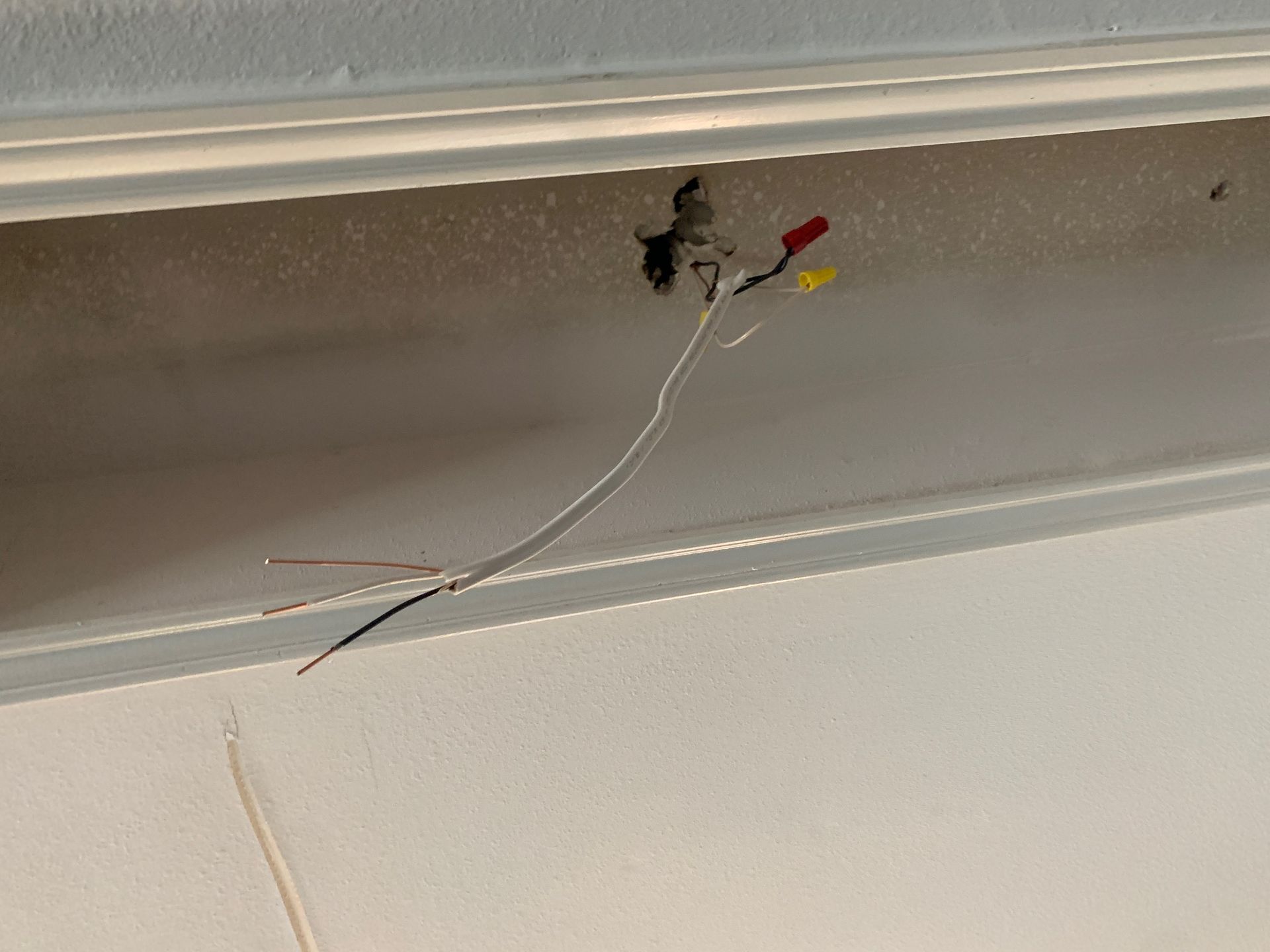 Exposed electrical wires hanging from a hole in the ceiling near trim.