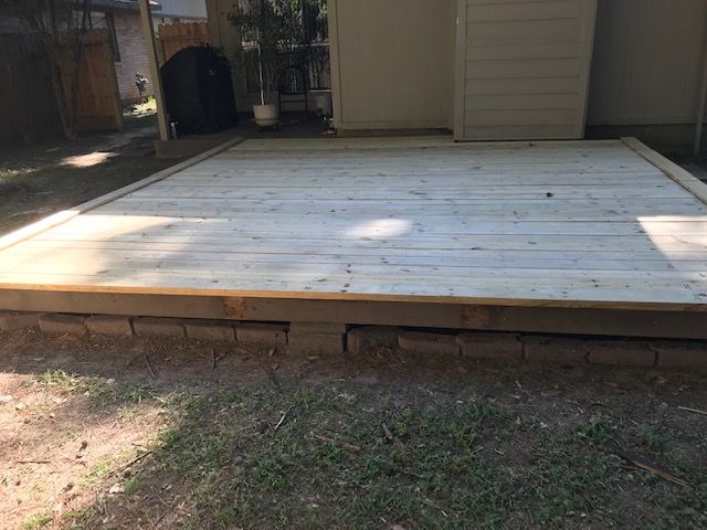 White wooden deck platform beside a beige house in a backyard, with grass in the foreground.