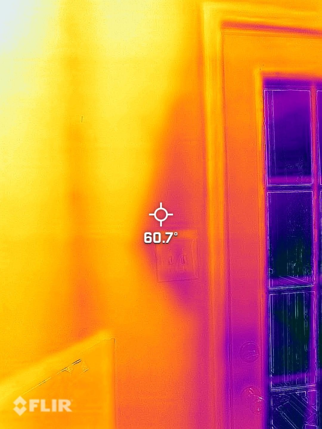 Thermal view of a person beside a window and wall, with a measured hotspot at 60.7°.