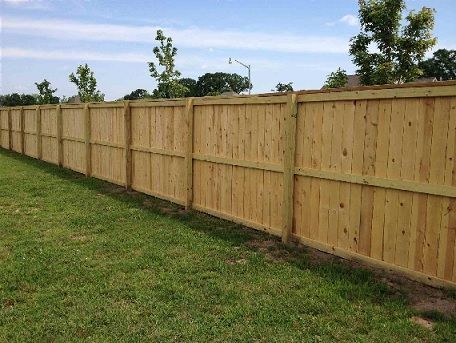 Long wooden privacy fence bordering a grassy yard under a blue sky