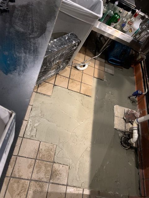 Narrow kitchen corridor with tiled floor, wet patch, sink area, and cleaning supplies.