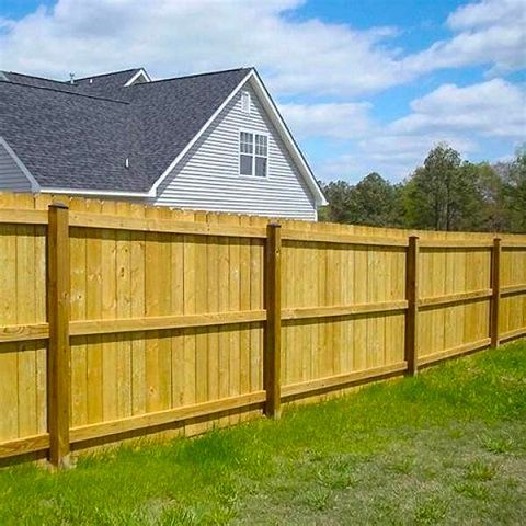 Wooden privacy fence beside a gray house on a grassy yard under a blue sky.