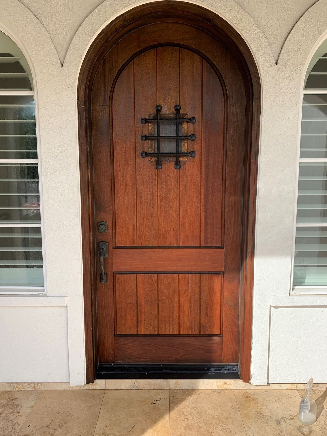 Wooden arched front door with black iron grille set in a cream stucco entryway