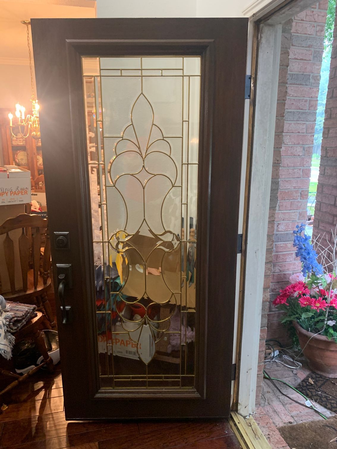 Dark wooden front door with decorative frosted glass panel, opening to a porch with potted flowers.