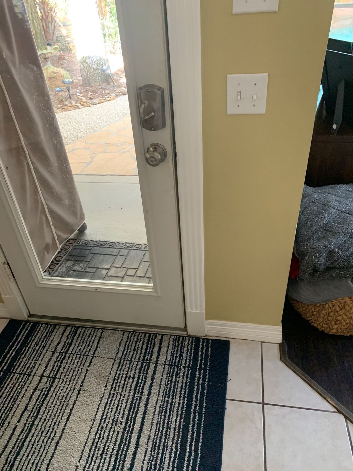White door with glass panel beside a tiled entryway, striped rug, and a light switch on a tan wall.