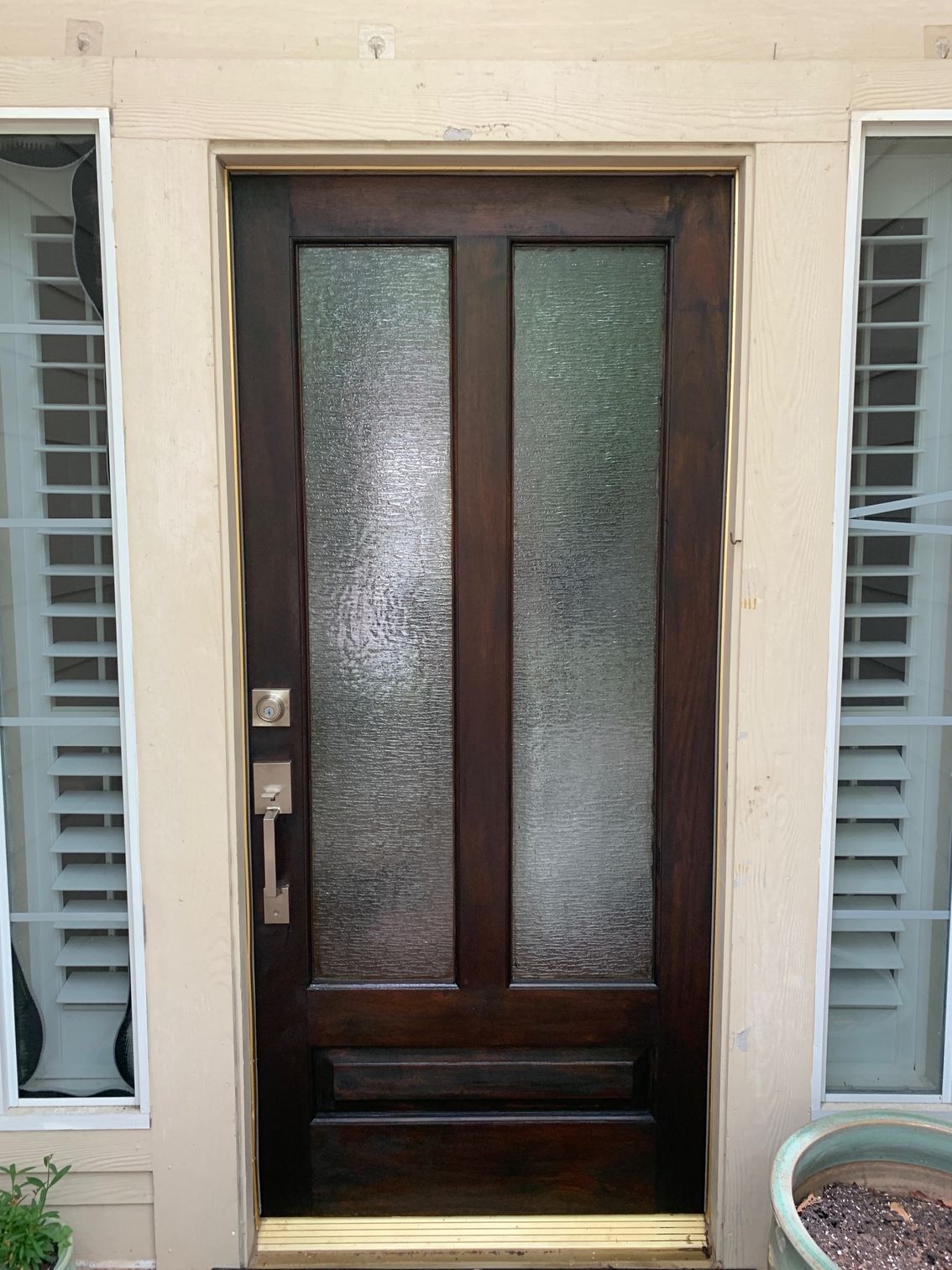 Dark wooden front door with frosted glass panels and sidelights on a beige exterior wall