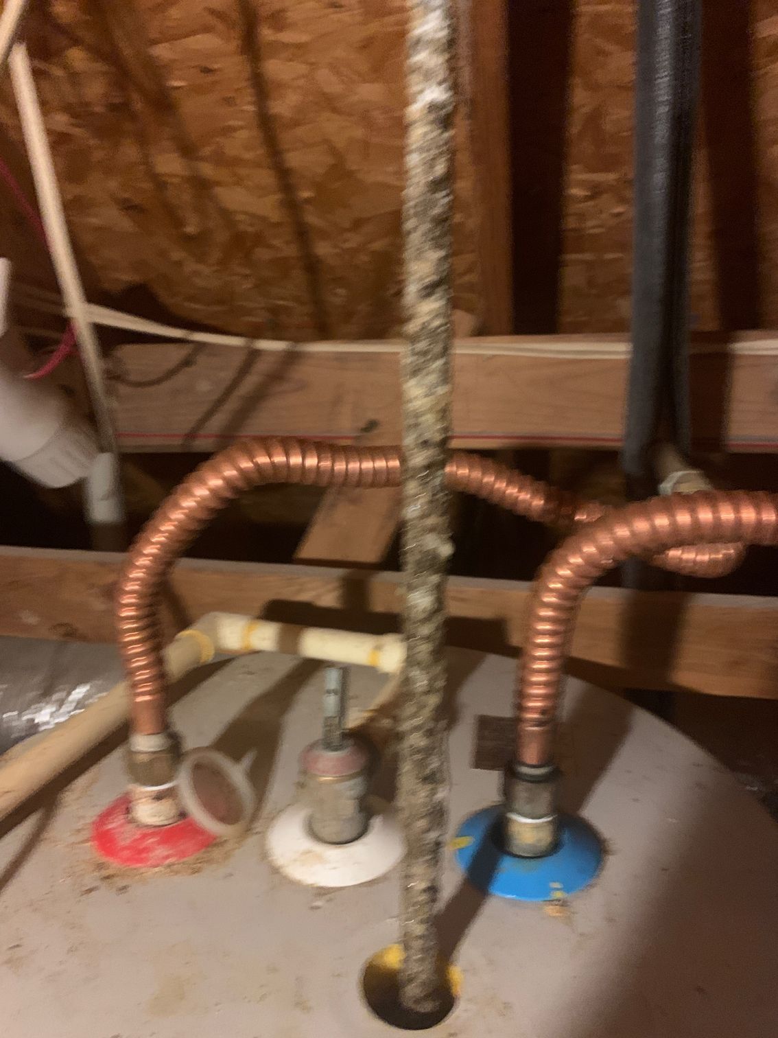 Plumbing under a sink with three copper water lines connected to colored valve fittings on a water heater or fixture