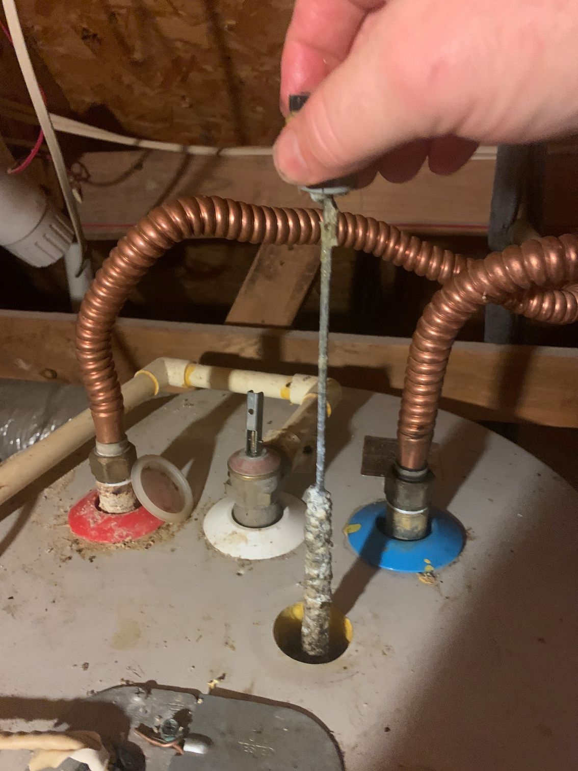 Hand holding a cable above copper pipes and colored floor openings in a utility area