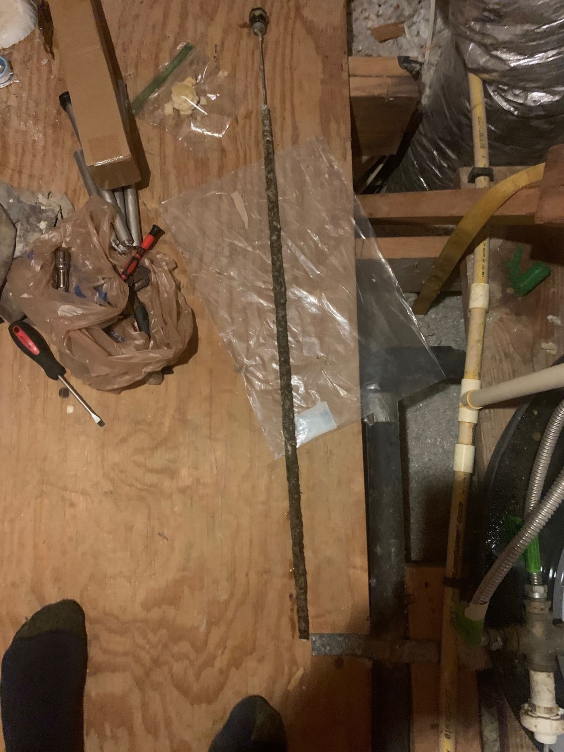 Cluttered attic floor with exposed wiring, ductwork, and wooden beams under plastic sheeting.