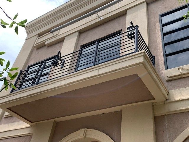 Balcony with black railings on a beige building exterior, viewed from below