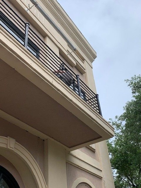 Low-angle view of a beige building facade with balconies and a large arched entrance beside a tree