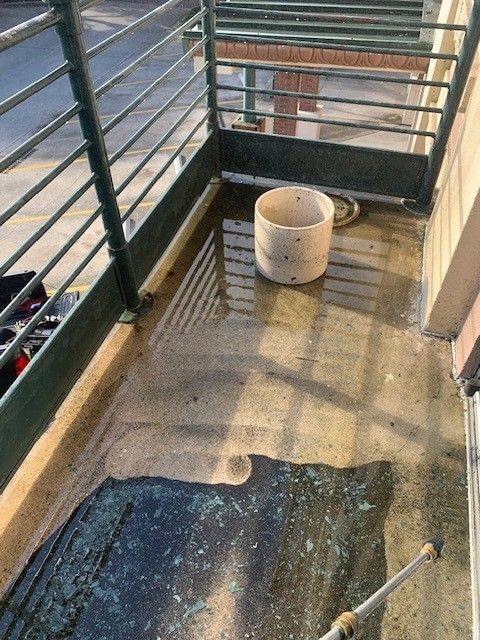 Balcony with wet floor, black mat, and white bucket near metal railing.