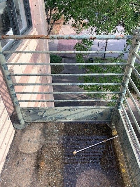 Wet balcony with metal railings, a narrow view of a courtyard below, and a small stick on the floor.