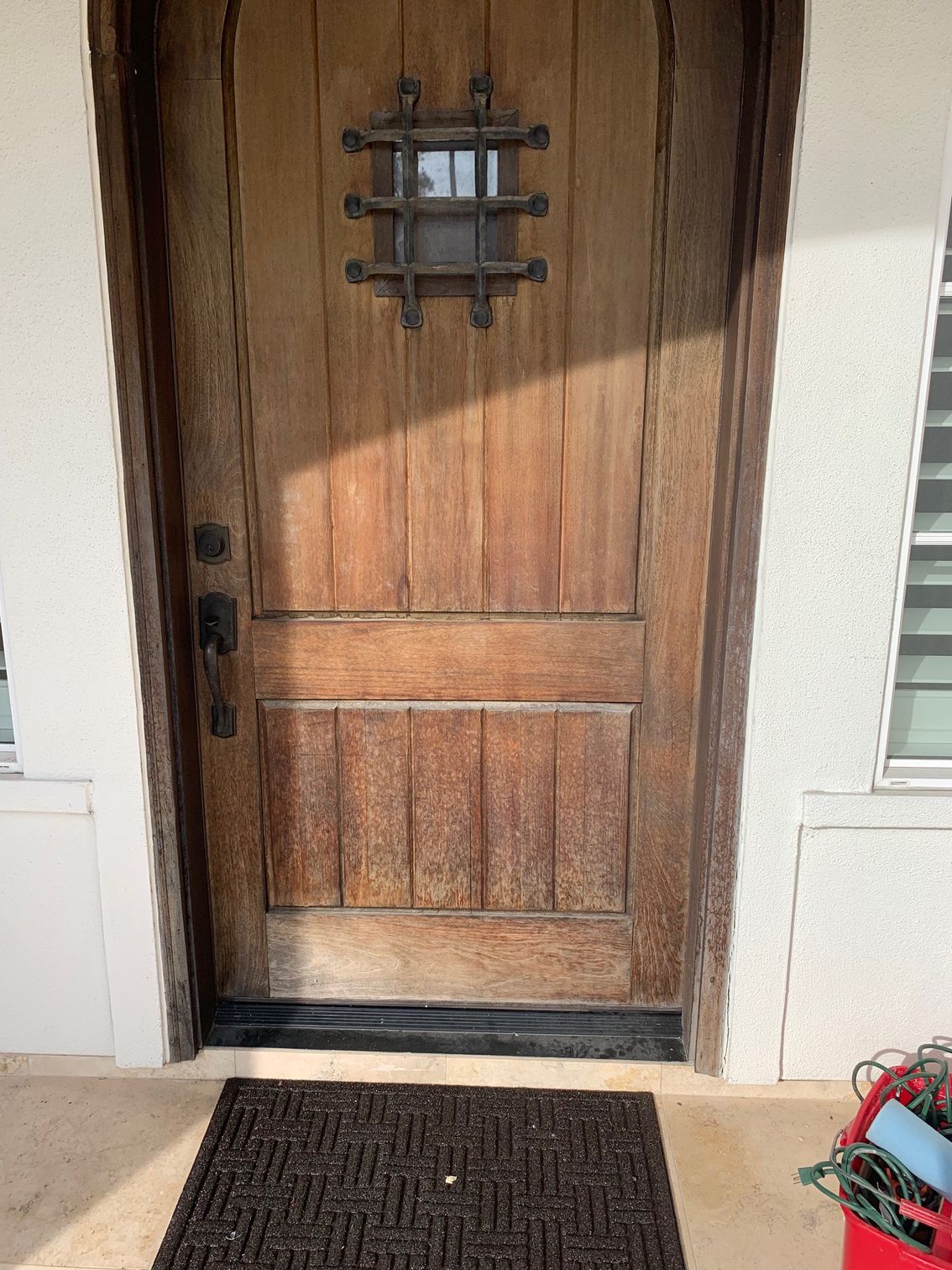 Wooden front door with a small barred window and doormat outside