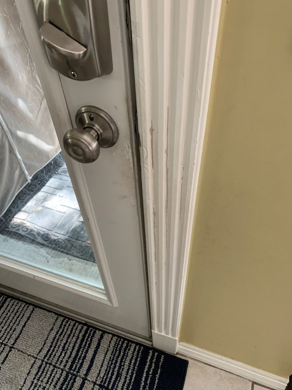 Close-up of a white door with silver handle and deadbolt, next to beige wall and striped carpet.
