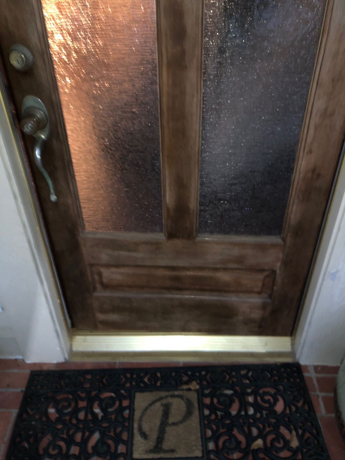 Wooden front door with frosted glass panels above a patterned doormat