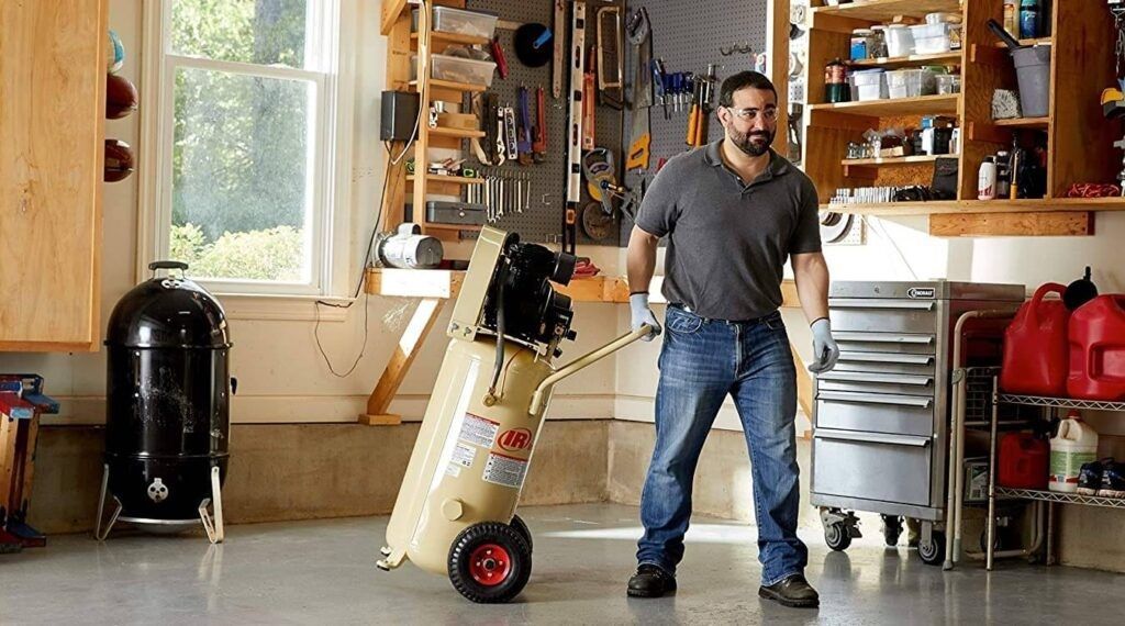 Man standing in a garage workshop beside a beige appliance, with tools and cabinets in the background
