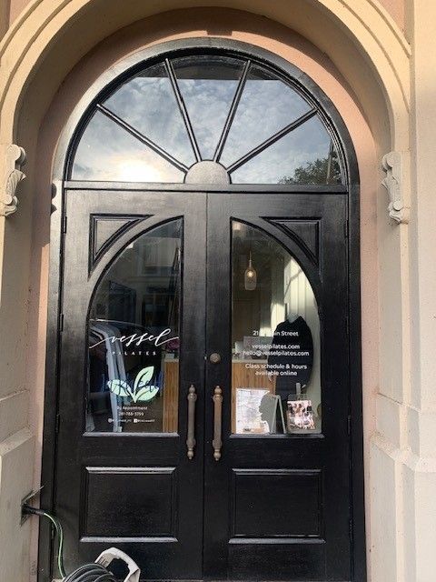 Black arched storefront doors with glass panels and white lettering under a stone archway.