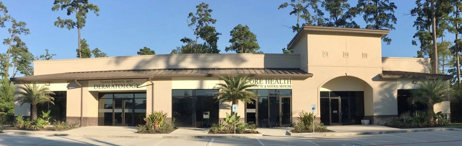 Tan stucco building with arched entrances, green awnings, and trees in front under a clear blue sky