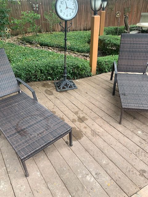 Backyard deck with two wicker lounge chairs and a freestanding clock by a wooden fence.