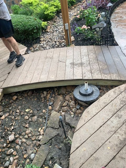 Wooden garden bridge over a rocky streambed, with a person standing at the left edge.