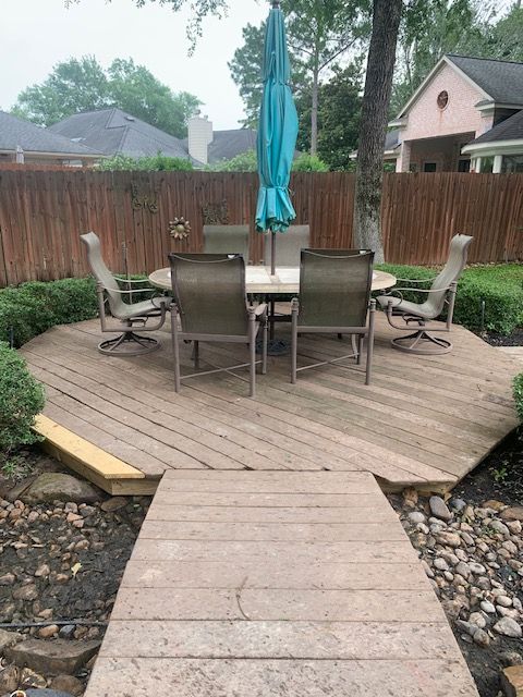 Wooden backyard deck with patio table, chairs, and closed teal umbrella behind a fenced walkway