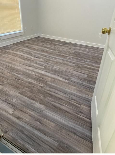 Empty room with gray wood-look flooring and white walls, seen from an open doorway.