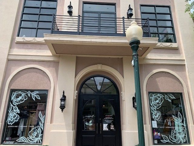 Two-story storefront with arched entrance, black balcony railings, and decorative window displays