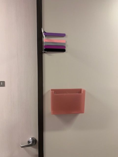 Wall-mounted organizer with purple, pink, and black slots above a pink bin beside a door handle.