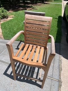 Wooden patio chair on a stone walkway beside a green lawn, lit by sunlight.