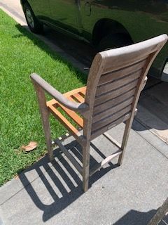 Wooden chair on a sunlit sidewalk beside a parked dark car and grassy lawn