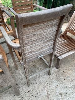 Weathered wooden patio chair centered on a concrete surface, with other chairs partially visible around it.
