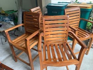 Three wooden patio chairs on a porch, with green storage bins in the background.