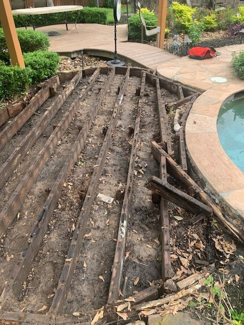 Damaged wooden deck over a pond in a garden patio, with broken planks and debris around the edge