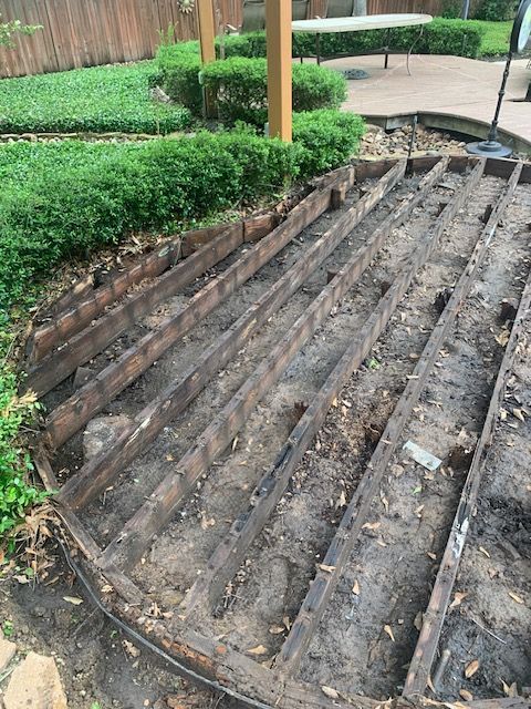 Sloped dirt planter bed with wooden beams beside trimmed hedges and a patio umbrella