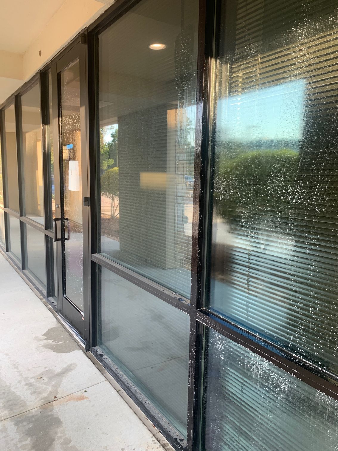 Row of dark-tinted glass storefront windows along a covered sidewalk with blinds inside