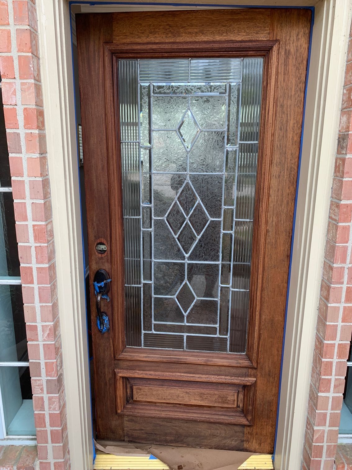 Wooden front door with decorative glass panel and black handle set in a brick wall