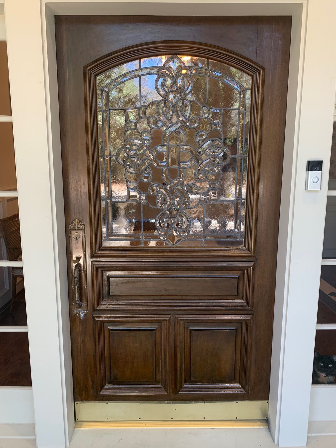 Ornate dark wooden front door with decorative glass panels in a white entryway