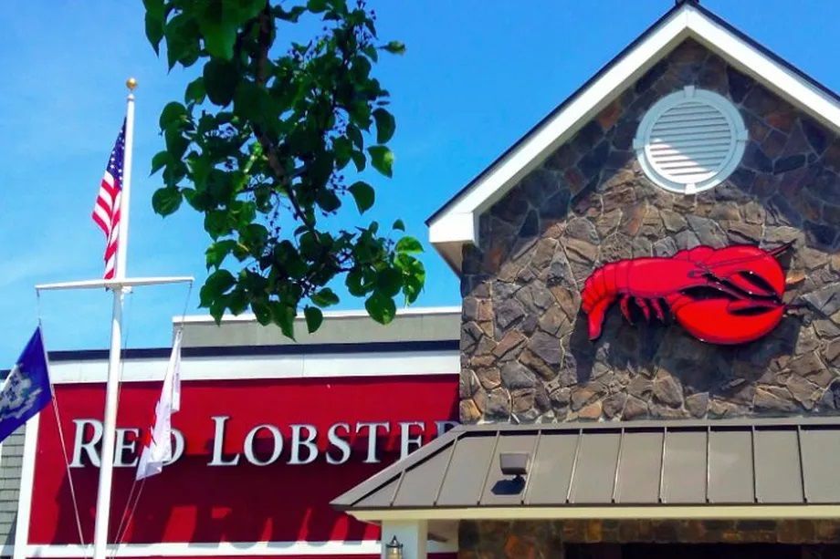 Red Lobster restaurant exterior with red signage and a large red lobster logo under a cloudy sky