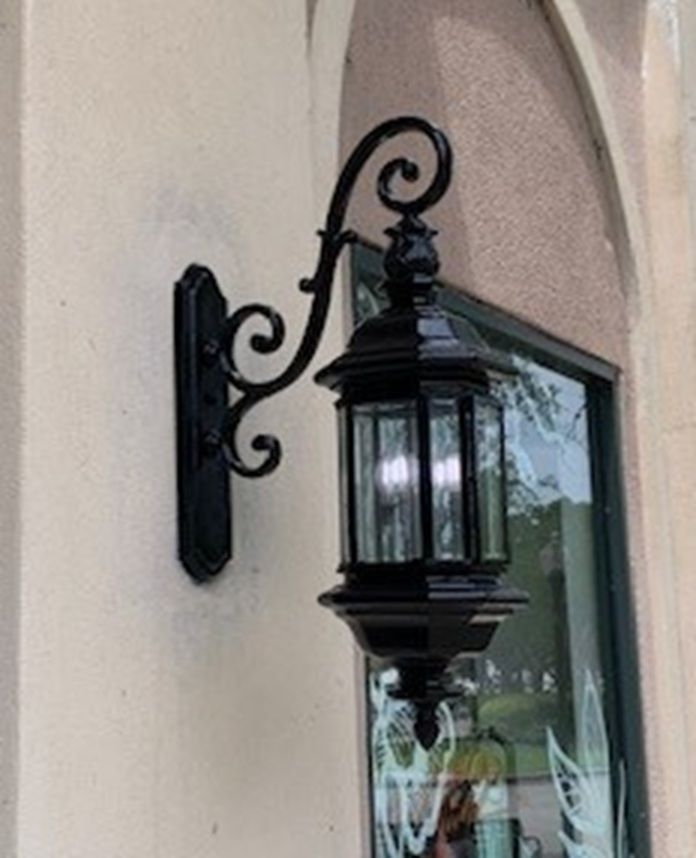 Black decorative wall lantern mounted beside a window on a beige exterior wall