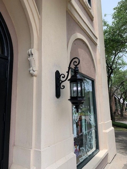 Exterior wall with a black lantern-style sconce beside an arched window on a beige building
