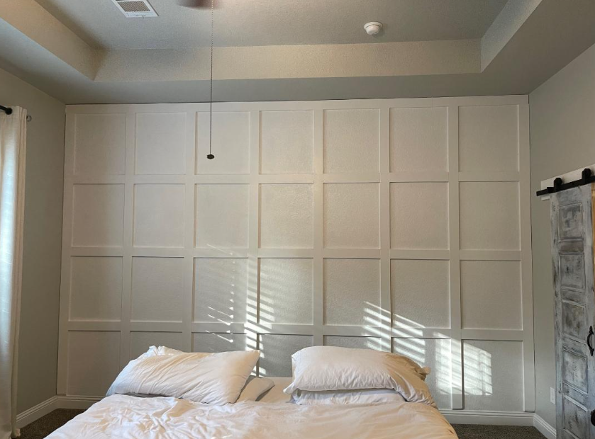 Minimal bedroom with white paneled wall, twin beds, and sunlight streaming through blinds