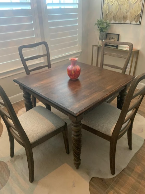Dining table with four chairs, a red vase centerpiece, and window blinds in a bright room