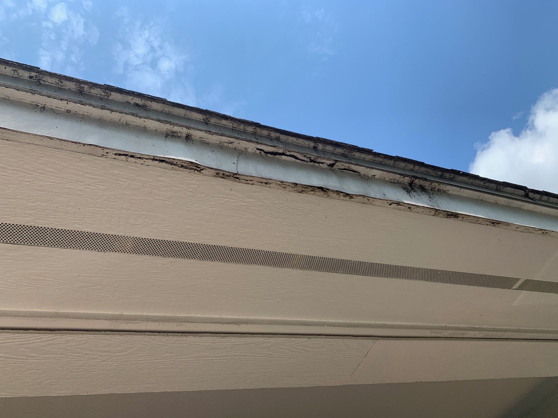 Close-up of beige house siding and roofline under a blue sky with clouds