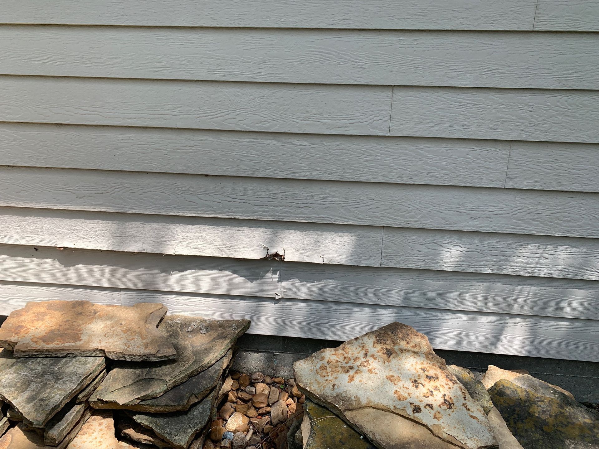 Stacked slate stones and rocks beside a gray house siding wall.