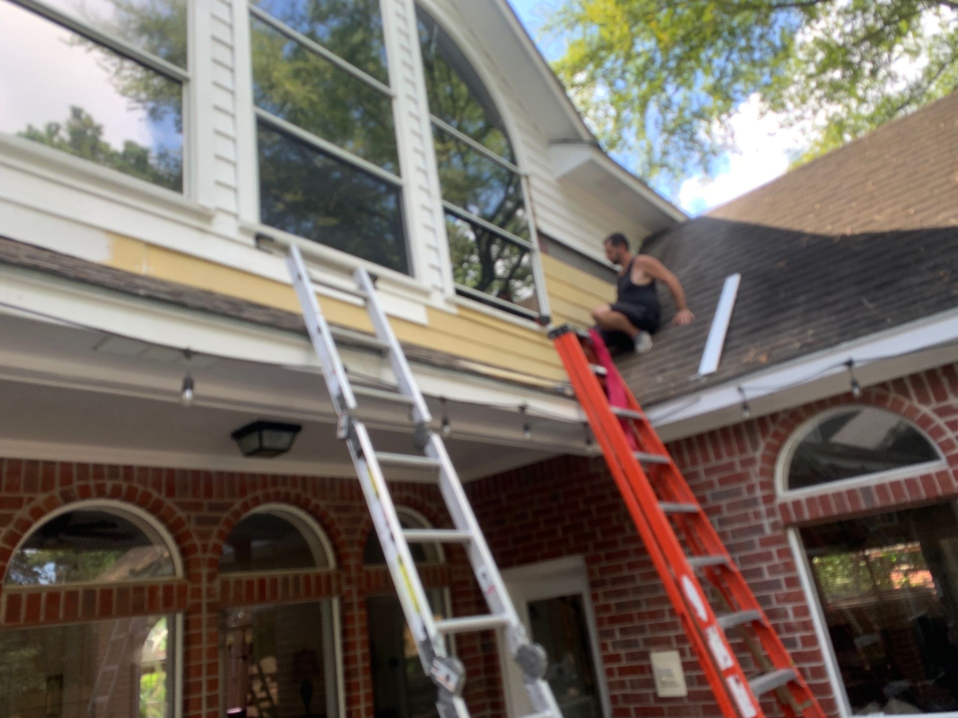 Person on red ladder repairing roof of a two-story brick house