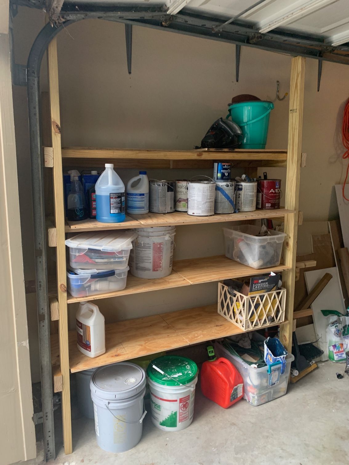 Shelves stocked with paint cans, bottles, and buckets in a garage or storage area
