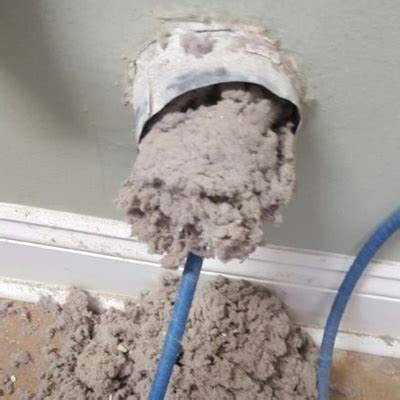 Crumbling white wall vent clogged with gray lint or debris, blue cable below it.